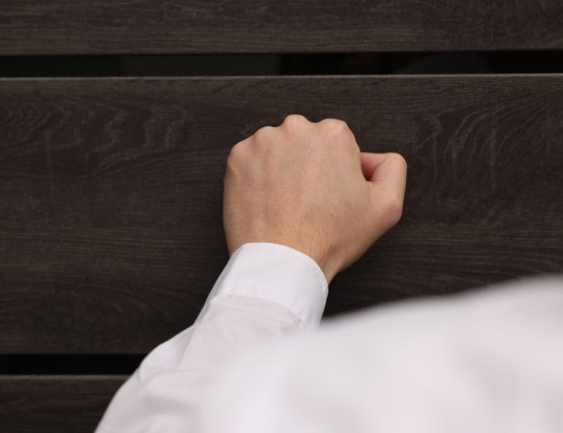 Photo of a person in a white shirt's arm, knocking on a door.