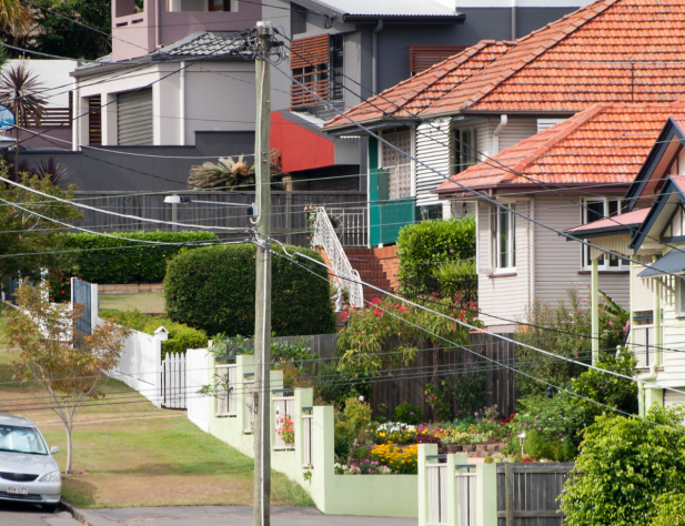 Photo of suburban Brisbane street, featuring power lines, a parked car and rows of houses.