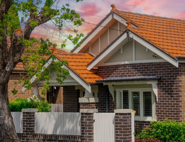 Photo of the front of a red brick house with terracotta tile roofing at dusk.