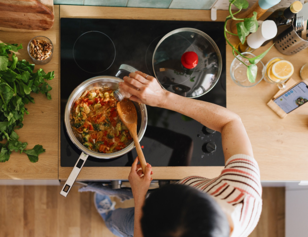 Photo taken from above, featuring a person using induction cooktop in a kitchen, surrounded by cooking implements and ingredients.
