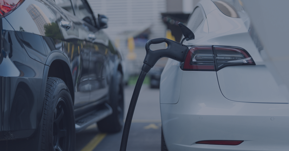 Close-up photograph of two cars; one is an electric vehicle (EV) charging, and you can see the charge cable in shot.